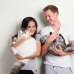 Young happy couple holding two cats together